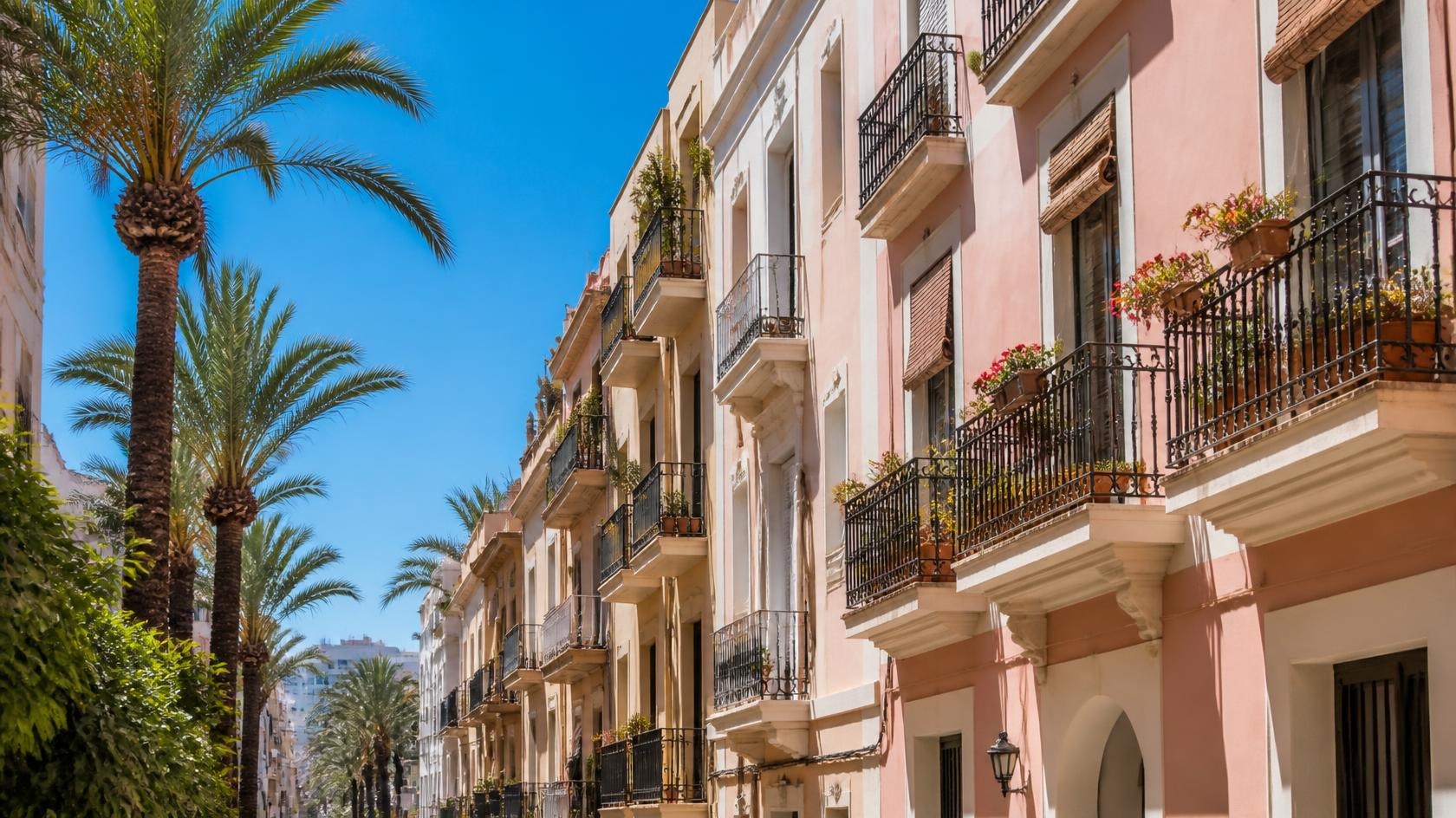 Sunny residential street in Alicante with pastel buildings, iron balconies and palm trees